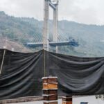 Bridge under construction with cranes in a picturesque mountain landscape.