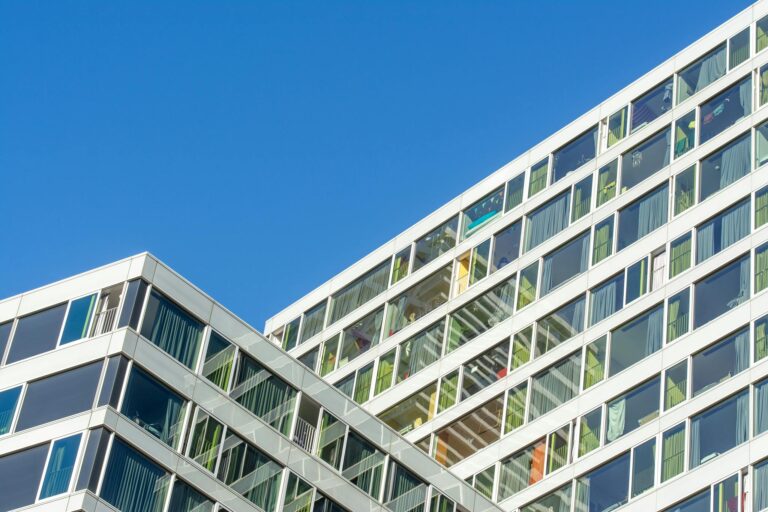 Contemporary glass facade of a modern building in Den Haag against a clear blue sky.