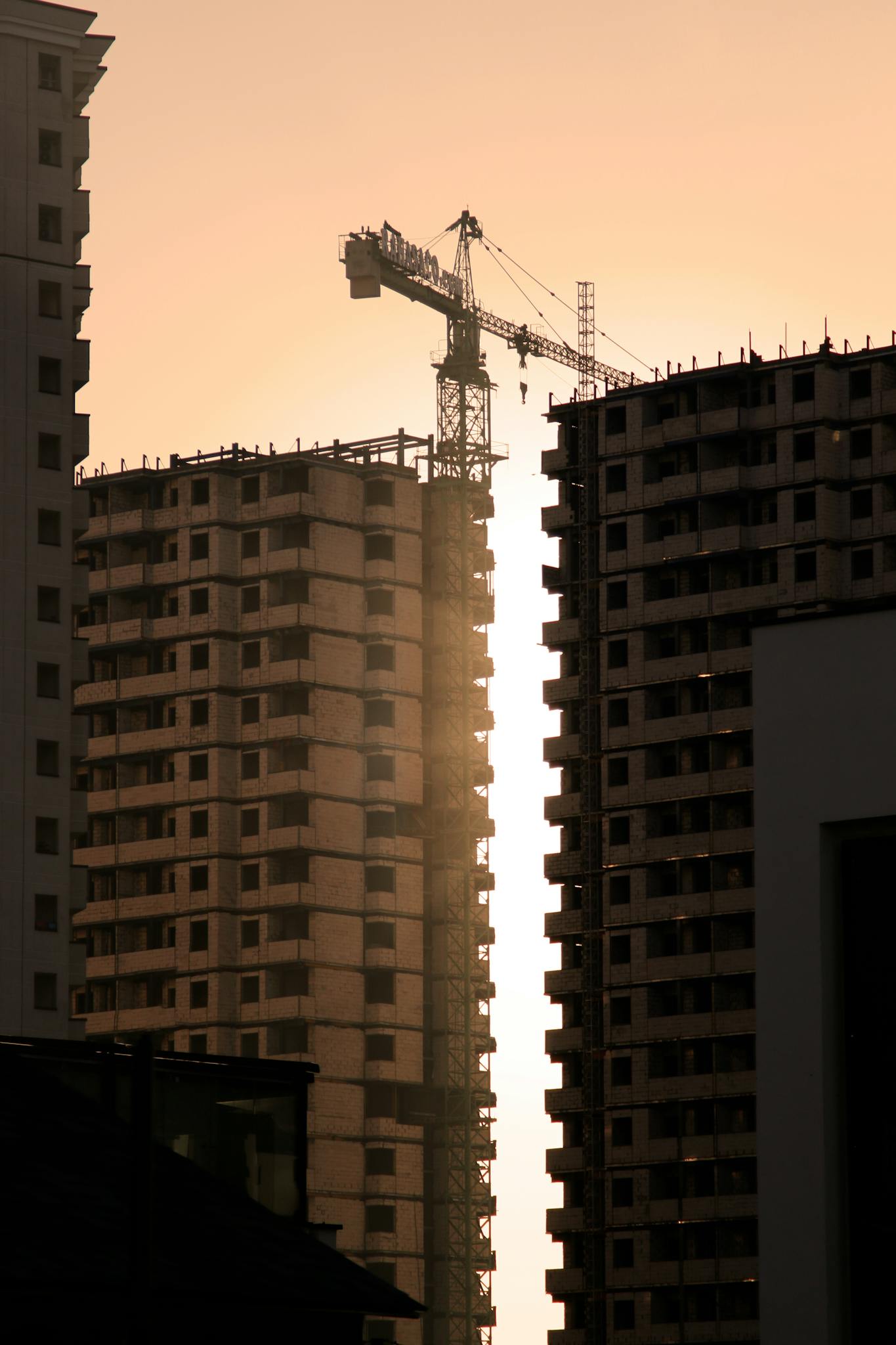 Silhouette of high-rise buildings under construction with a crane at sunset, showcasing urban development.