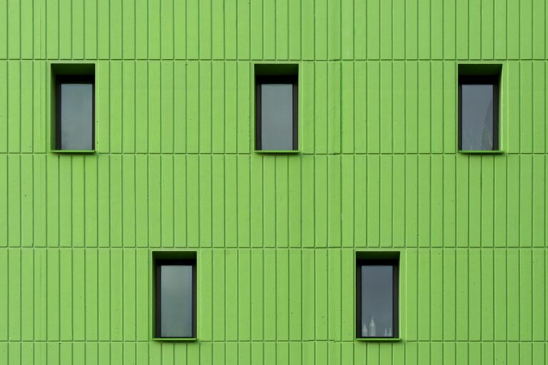 Vibrant green building facade with symmetrical black-framed windows.